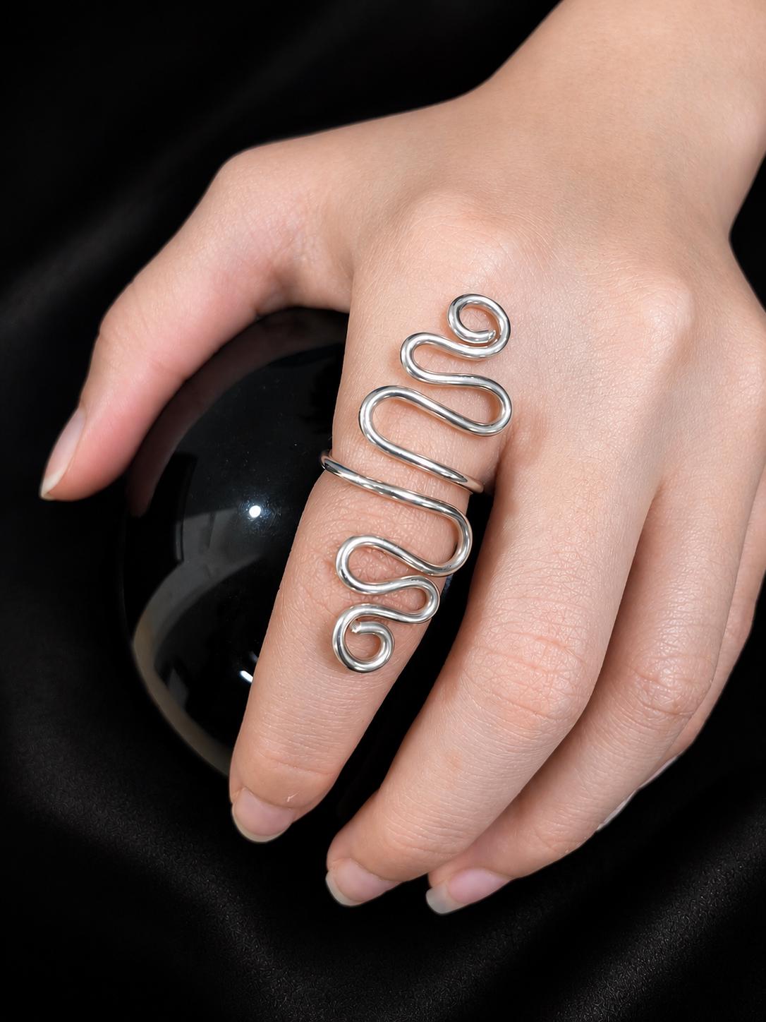 The Serpentine ring, a single unbroken strand of silver flowing across the finger and ending in two spirals.